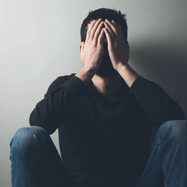 A man sits with his head in his hands representing What Are the Signs a Man Might Be Suffering in Silence?