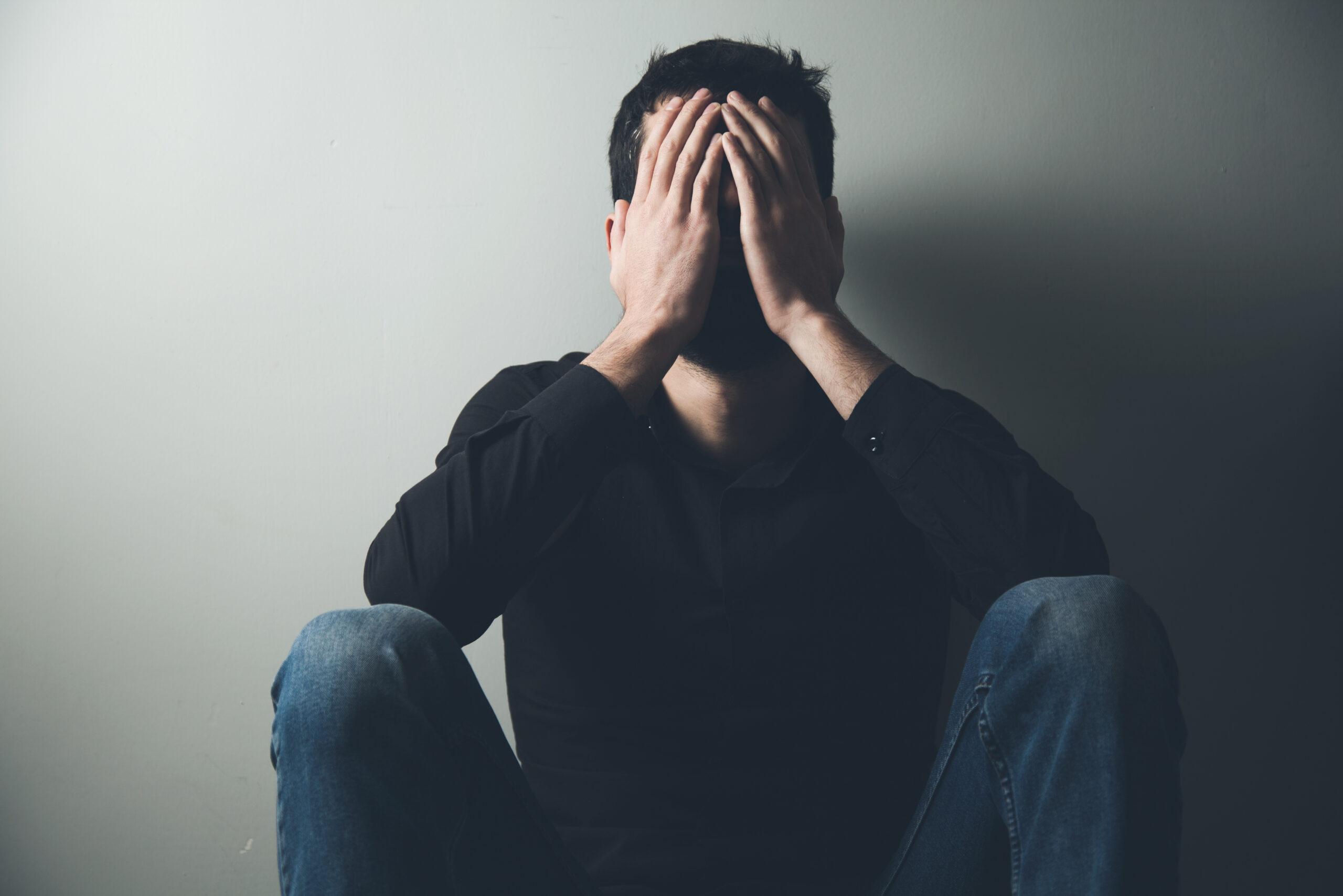 A man sits with his head in his hands representing What Are the Signs a Man Might Be Suffering in Silence?