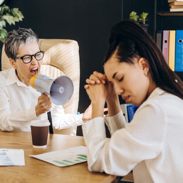 Employee stressed at desk while bully boss yells through megaphone in toxic workplace