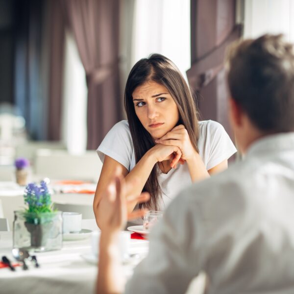 Woman looking uncomfortable while listening to her partner during a tense conversation at a restaurant, illustrating the experience of getting the ick in relationships.