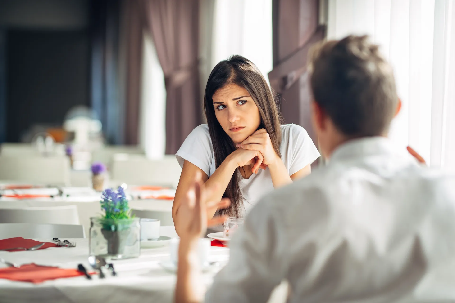 Woman looking uncomfortable while listening to her partner during a tense conversation at a restaurant, illustrating the experience of getting the ick in relationships.