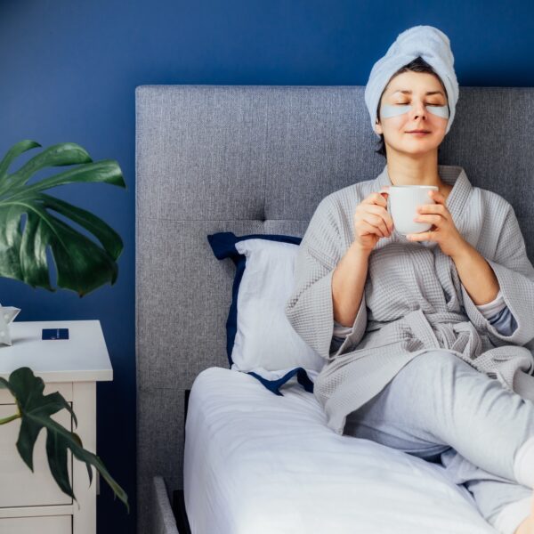 Counselor practicing self-care at home, relaxing in bed with tea and eye patches as part of a well-being routine.