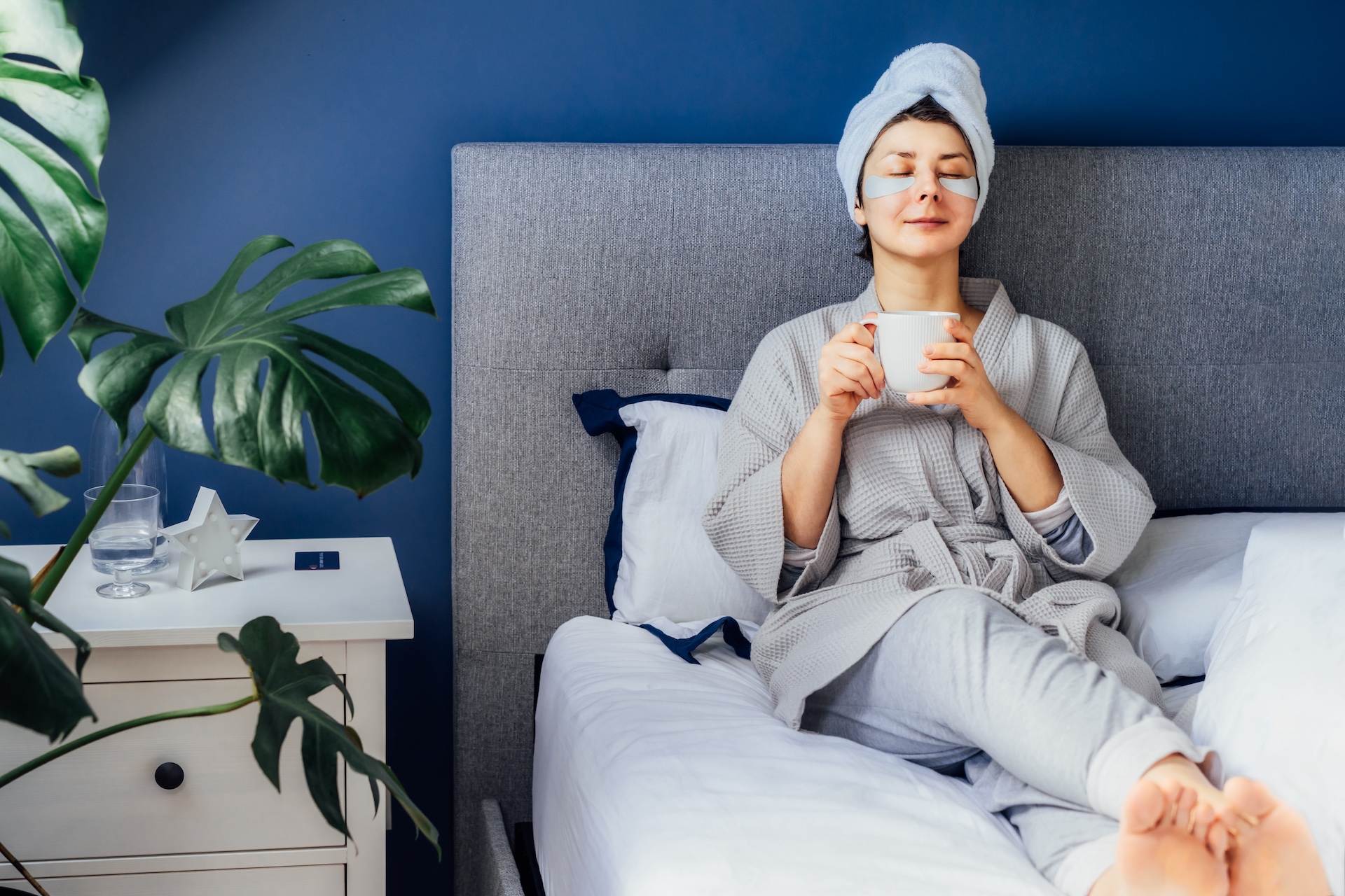 Counselor practicing self-care at home, relaxing in bed with tea and eye patches as part of a well-being routine.