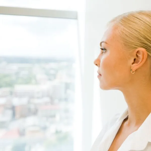 High achiever woman looking out the office window, reflecting on relationship and personal growth challenges.