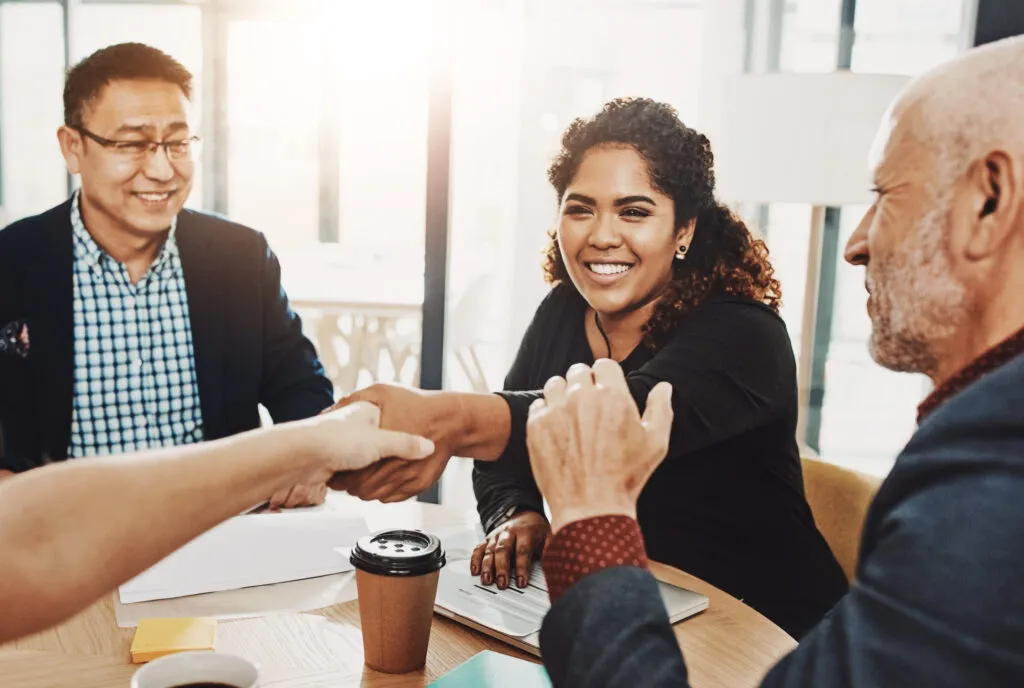 Smiling woman shaking hands in a business meeting, symbolizing trust, connection, and influential leadership.