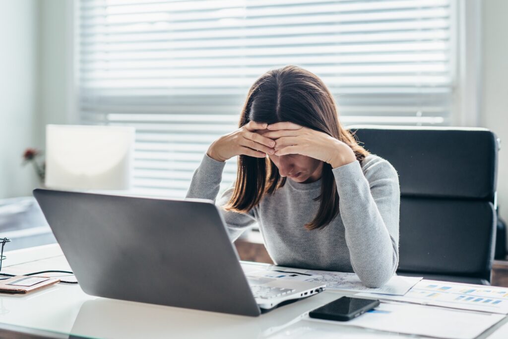 Stressed therapist sitting at desk with head in hands while working on laptop, symbolizing burnout and questioning when to exit the therapy profession.