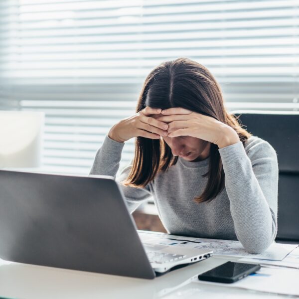 Stressed therapist sitting at desk with head in hands while working on laptop, symbolizing burnout and questioning when to exit the therapy profession.
