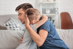 Father hugging his young son at home after an emotional moment, showing love, empathy, and how to deal with guilt in relationships.