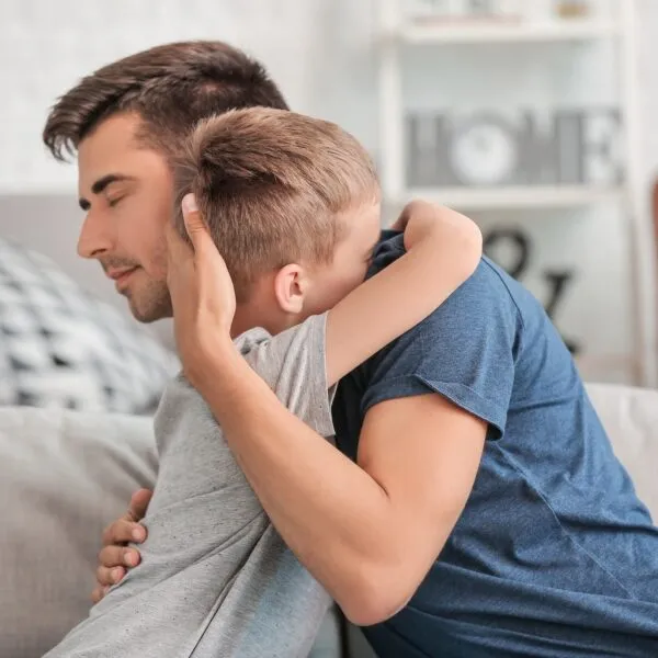 Father hugging his young son at home after an emotional moment, showing love, empathy, and how to deal with guilt in relationships.