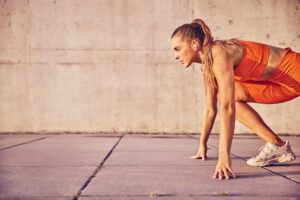 Woman in bright orange athletic wear preparing to sprint, symbolizing energy and focus.