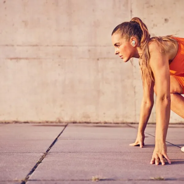 Woman in bright orange athletic wear preparing to sprint, symbolizing energy and focus.