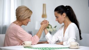 A younger woman and her mother-in-law arm wrestle at a table, symbolizing conflict and power struggles in a toxic mother-in-law relationship.