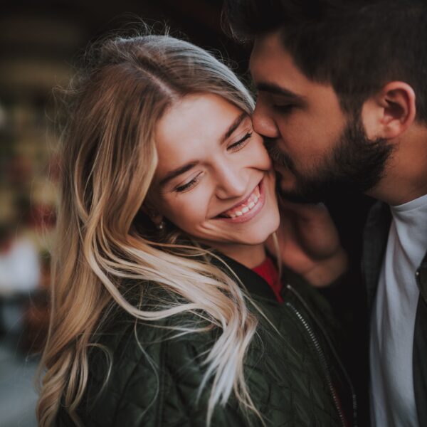 A smiling couple shares a warm, affectionate moment outdoors, illustrating emotional connection and intimacy in a romantic relationship.