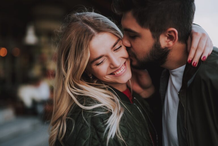 A smiling couple shares a warm, affectionate moment outdoors, illustrating emotional connection and intimacy in a romantic relationship.