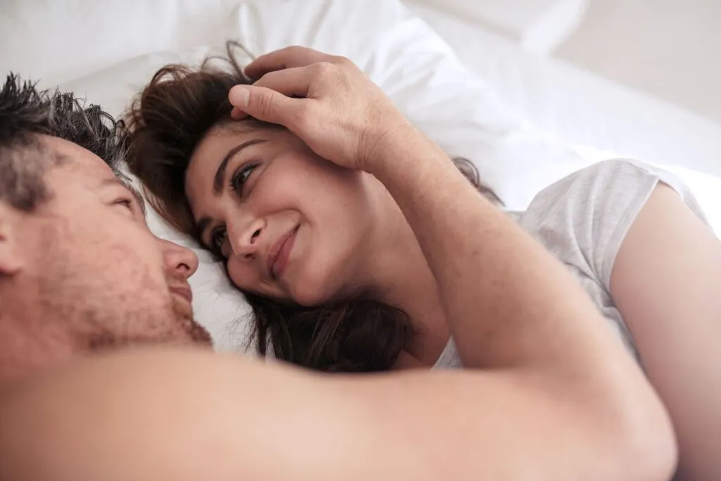 Couple lying in bed making eye contact and smiling, representing intimacy in marriage and reconnecting sexually