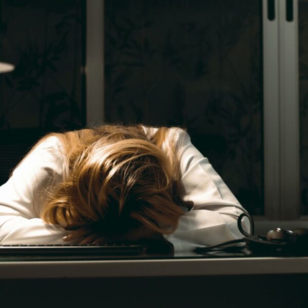 Woman with head down on desk at night, exhausted from stress and burnout while working on a computer.