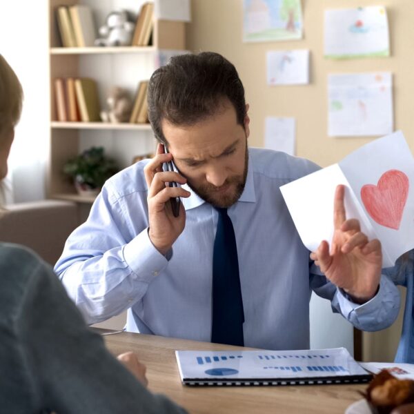 Father on a work phone call at home while his daughter shows him a drawing, illustrating the need to set boundaries at work and protect personal life