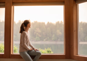 Woman sitting by a large window, looking out at a hazy landscape, reflecting climate anxiety and uncertainty.