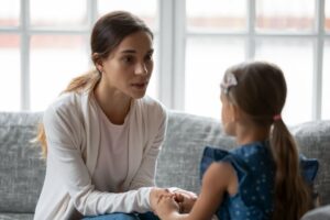 Parent holding a child’s hands during a calm conversation on a couch, illustrating emotion coaching and secure attachment parenting.