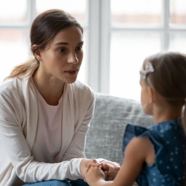 Parent holding a child’s hands during a calm conversation on a couch, illustrating emotion coaching and secure attachment parenting.